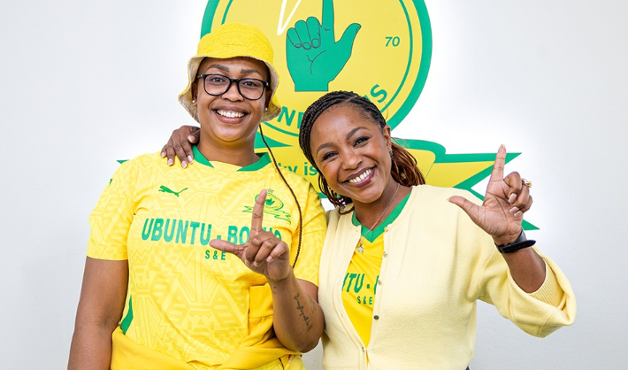 Two Mamelodi Sundowns supporters smiling and making the club hand sign